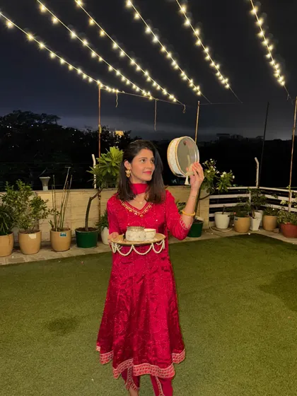 Celebrating Karwa Chauth on our terrace. I'm holding the traditional thali and sieve in a beautiful red embroidered anarkali suit, a classic choice for this festival.