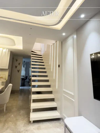 The 'after' shot of a staircase transformation in Amar Colony. The final design is clean, white, and modern, with integrated lighting along the wall that makes it a true architectural feature.