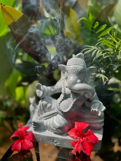 This reclining Ganesha statue, adorned with red hibiscus flowers, brings an aura of peace and success to any space it inhabits.