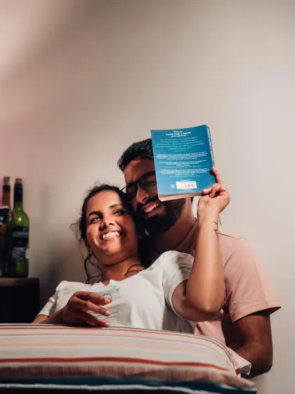 A playful indoor pre-wedding moment, with the couple sharing a laugh while reading a book together.