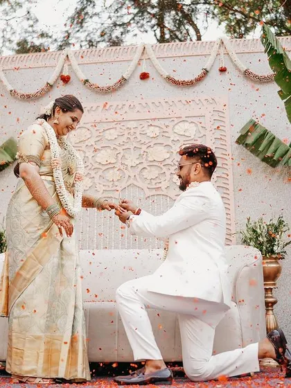 The groom gets on one knee in this beautiful moment, set against our elegant, traditionally inspired white backdrop with banana plant accents.