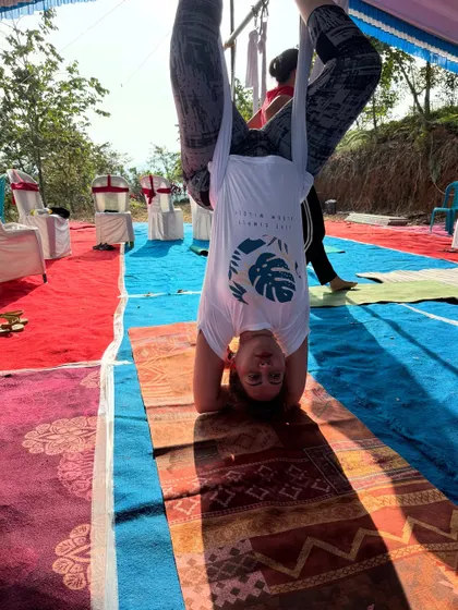 A participant in a supported headstand. The silk provides a safety net, allowing students to explore advanced poses they might not be ready for on the mat.