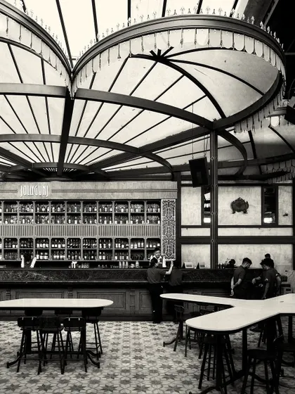 The main bar area with its unique tables and high stools. The patterned floor and grand light fixtures are prominent in this grayscale shot.