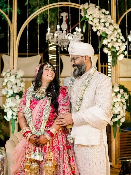 A classic portrait of the newly married couple on their wedding stage. The grand decor with white flowers and chandeliers provides a stunning backdrop for their first official photo together.