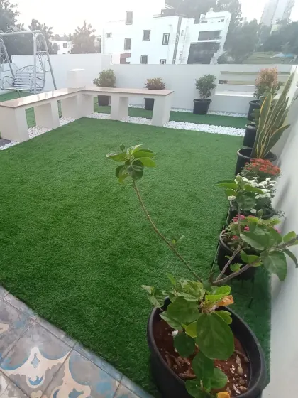 This perspective highlights the different zones of the rooftop garden, from the lawn area to the tiled patio space, all complemented by potted plants.