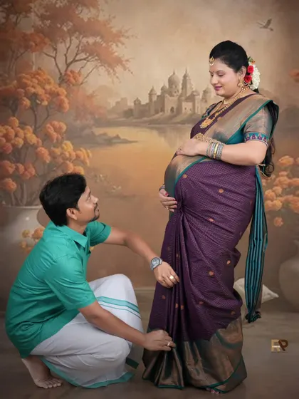 A sweet family moment. The dad-to-be kneels to adjust his partner's saree, while their older son looks on, creating a heartwarming traditional family portrait.
