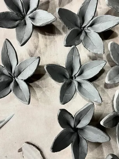 A collection of clay blossoms, each petal individually shaped by hand. These are waiting to be fired and glazed, and can be used as wall decor or incorporated into larger sculptural pieces.