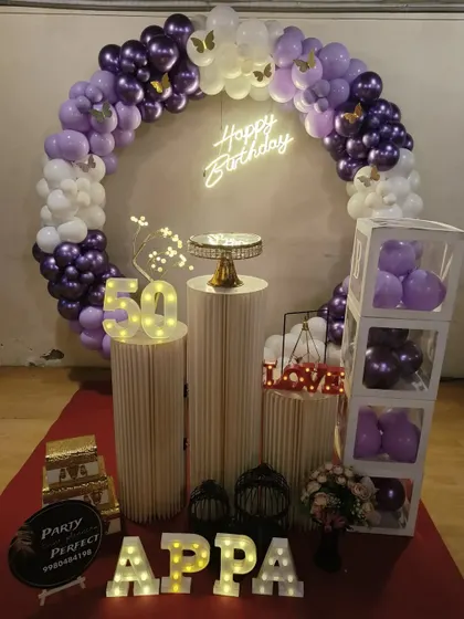 Celebrating a 50th birthday calls for something special and elegant. This setup features a purple and white balloon ring, a light-up marquee '50', custom illuminated lettering for 'APPA', and decorative props like birdcages, all designed to create a classy and memorable event.
