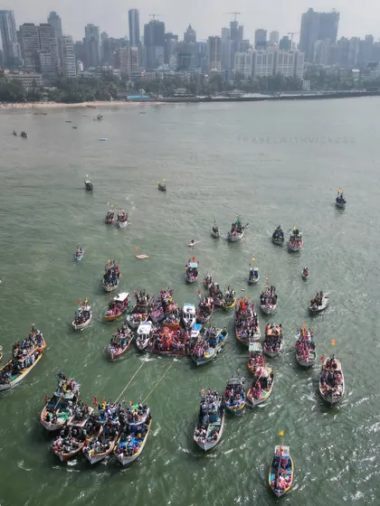 A wide aerial shot showing dozens of boats gathering in the Arabian Sea for the immersion of Lalbaugcha Raja. This perspective highlights the maritime aspect of the Visarjan against the backdrop of the Mumbai skyline.