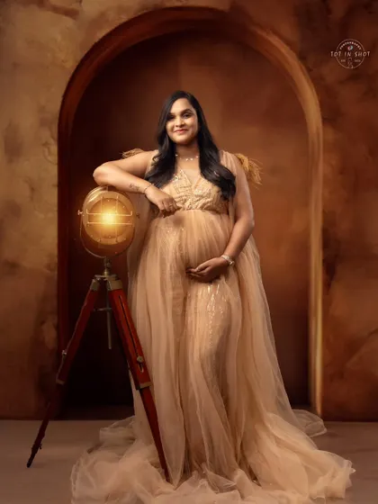 A regal portrait of an expecting mother in a golden gown, posing with a vintage globe to symbolize the world she's bringing a new life into.