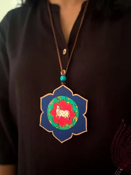 This lotus-shaped pendant features a miniature painting of a Pichwai cow, a sacred symbol in Indian art. The deep blue border makes the central motif stand out beautifully.