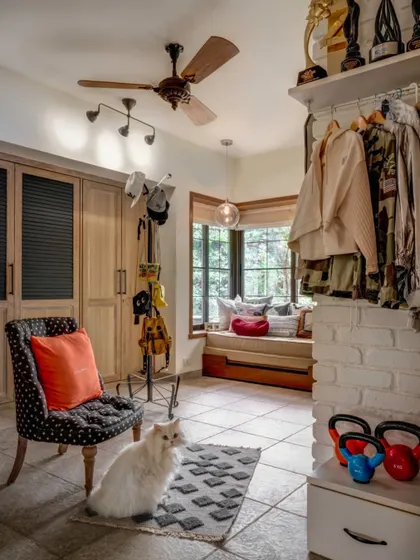 A walk-in closet and dressing area in Alia's home, complete with a cozy reading nook by the window. The space is designed to be practical yet personal, with a mix of open and closed storage to display her achievements and keep things organized.