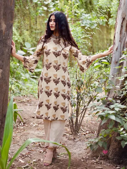 Set against a lush, green backdrop, this image makes the earthy tones of the printed kurta pop. The model's pose is open and inviting, highlighting the flared sleeves and A-line cut, which are important selling points for this design.