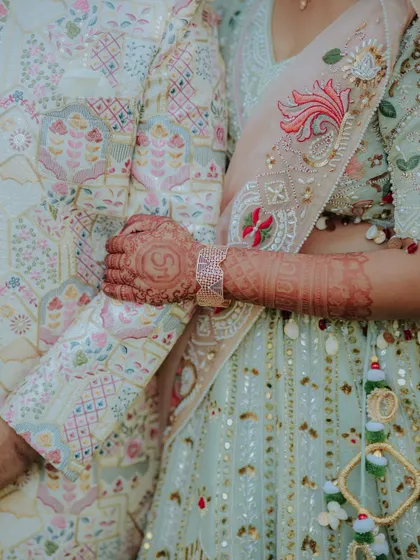 A close-up on the details. This shot focuses on the bride's henna-adorned hand resting on the groom's intricately embroidered sleeve, a symbol of their union.