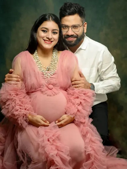 A happy and classic portrait of an expecting couple. The mom-to-be looks radiant in her pink gown, and they both smile warmly at the camera.