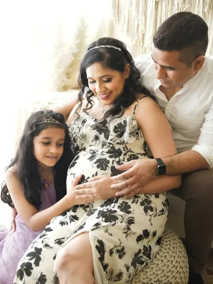 This shot shows a complete family maternity session, with the older sister sharing her excitement. The bright, natural light from the window creates a soft and gentle mood.