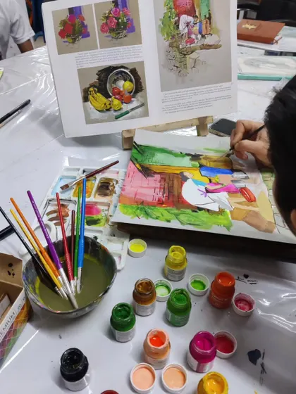 An overhead view of the student's workspace, showing the array of gouache colors and brushes used to create the vibrant composition.