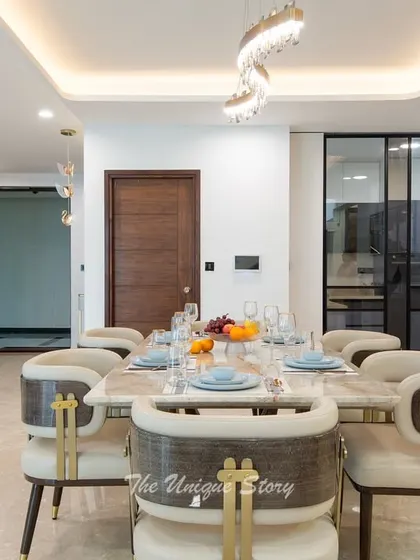 This view of the dining area shows its connection to the kitchen through a sleek glass partition. The elegant dining chairs with gold accents and the modern chandelier create a luxurious atmosphere for entertaining.