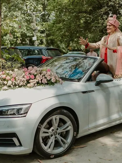 The groom makes a stylish entry in a white convertible Audi, decorated with a garland of pastel roses.