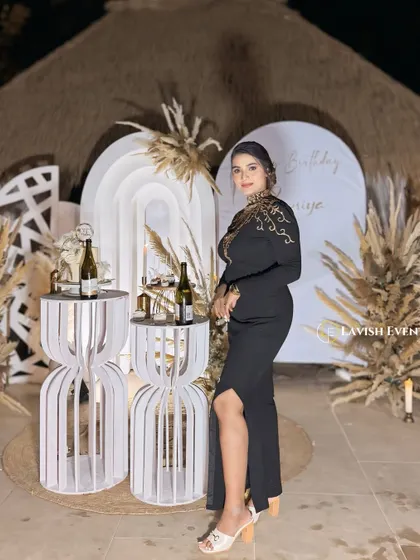 The birthday girl posing in front of her elegant boho-themed decor. The natural textures of the thatched roof and pampas grass complement her stylish look perfectly.