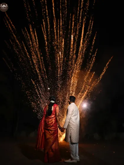 A dramatic shot of a couple holding hands, their backs to the camera, as they watch a display of ground-level fireworks. This image captures the grand celebration of their union.