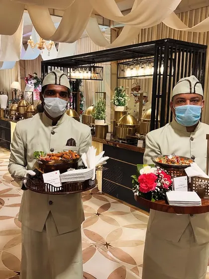 Our attentive staff are a key part of the experience. Here, two of our team members present trays of freshly prepared appetizers within a grand, beautifully decorated wedding hall, showcasing our commitment to seamless service.