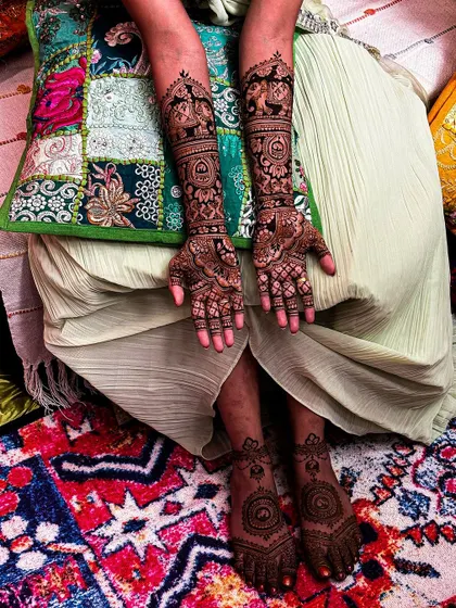 A full view of Mayuri's bridal mehendi on both hands and feet, set against a vibrant, colorful backdrop.