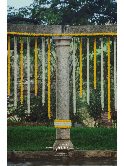 A close-up of a stone pillar adorned with marigold and chrysanthemum garlands, a simple yet elegant detail.