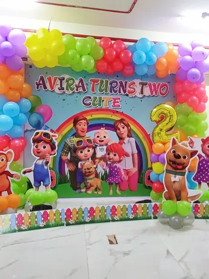 A full Cocomelon themed decoration for a second birthday party, perfect for toddlers. This setup includes a large, colorful backdrop with the entire Cocomelon family and friends, framed by a vibrant balloon garland. Life-sized character cutouts of JJ, TomTom, YoYo, and their animal friends bring the theme to life, making it an immersive experience for the little ones.