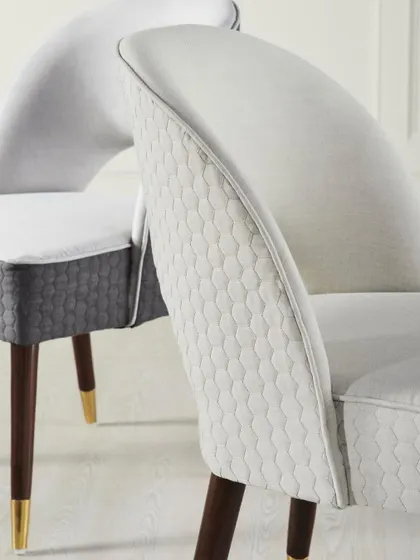 A detail shot showing the back of the dining chairs. This angle emphasizes the quilted fabric and the contrast between the light upholstery and dark wooden legs.