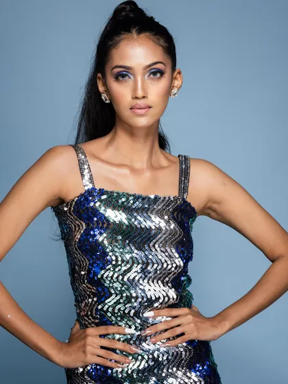 A confident pose in a blue and green sequin dress against a blue backdrop.