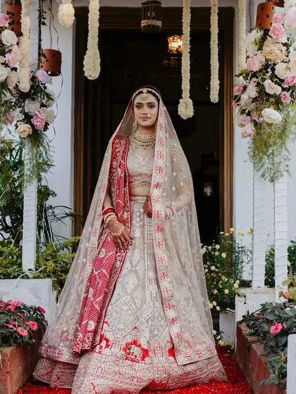 The bride standing at the entrance of her home, ready to begin her new journey. The red rose petal carpet adds a touch of classic romance.