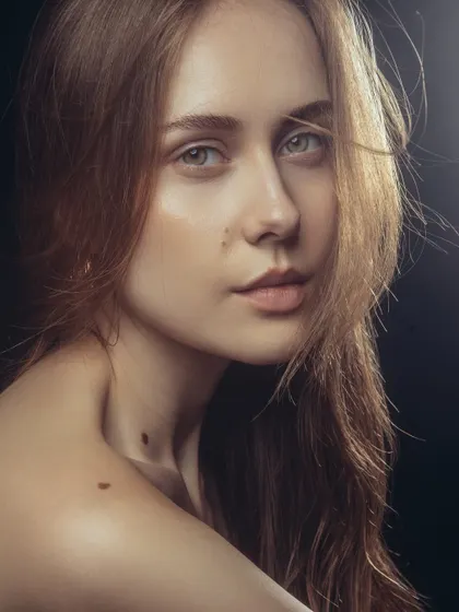 A close-up beauty portrait against a dark background, which makes the highlighted, dewy skin pop.