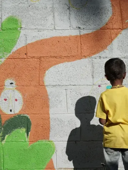 A young boy in a yellow shirt stands back to admire the work in progress. These moments of reflection are just as important as the act of painting, allowing the kids to see how their individual efforts contribute to a big, beautiful whole.