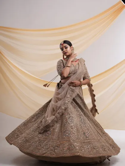 A beautiful beige lehenga with detailed embroidery, captured in a twirling motion to show the full, flowing skirt. A perfect outfit for a sangeet or reception.