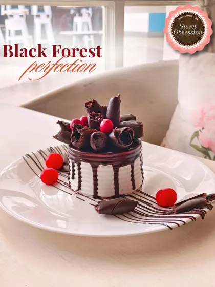A classic Black Forest pastry, reimagined. This individual portion features layers of chocolate sponge, cream, and cherries, beautifully decorated with chocolate curls.