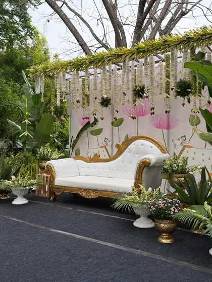 A modern and fresh take on a baby shower, with a Pichwai-inspired backdrop surrounded by lush greenery and banana plants for a tropical, traditional feel.