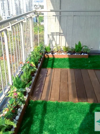 For this high-rise apartment balcony, I focused on creating a clean, green border. Planters filled with a variety of low-maintenance plants line the railing, set on a combination of artificial grass and wooden deck flooring. This design maximizes floor space while offering a beautiful view from inside.