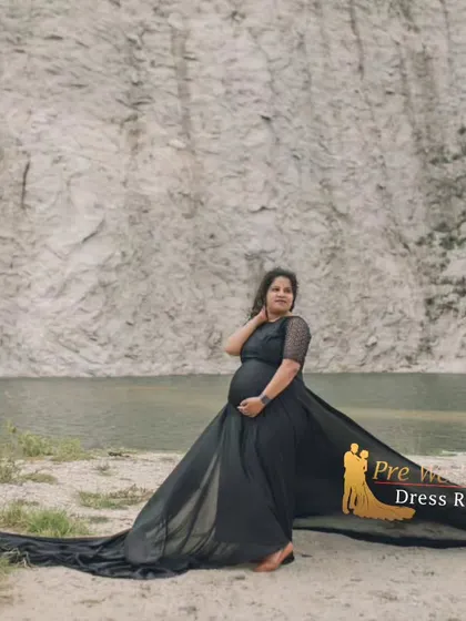 The black flying tail gown stands out against a rugged, natural cliffside. This image showcases how the gown's long train can be spread out to create a dramatic, grounded effect for your maternity photos.