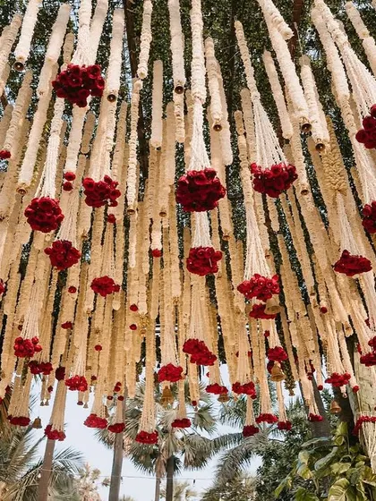 A view from below the mandap canopy, showing the dense arrangement of hanging tuberose and red rose clusters.