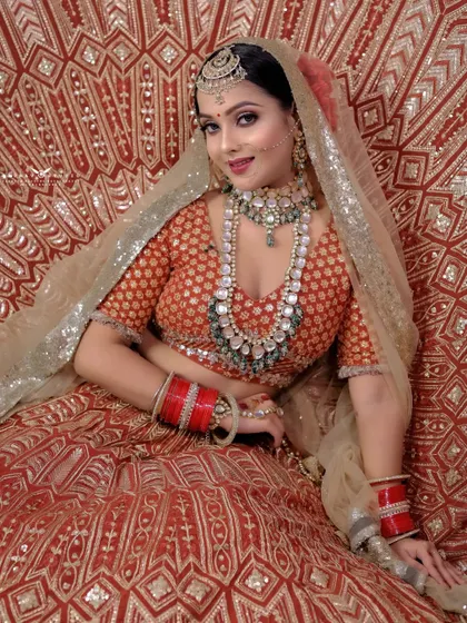 A beautiful shot of the bride seated against a richly patterned red and gold backdrop. The composition makes her red lehenga blend seamlessly, creating a truly opulent look.