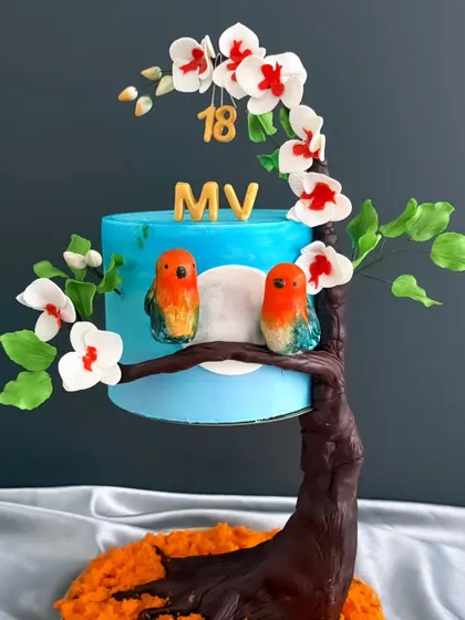 A delightful blend of artistry and deliciousness. This gravity-defying cake features two lovebirds perched on a branch of a flowering tree, perfect for an 18th birthday.