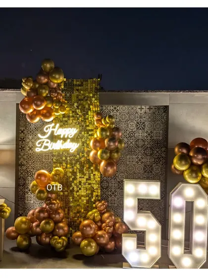 Celebrating 50 golden years! This glamorous outdoor setup features a gold sequin wall, large light-up numbers, and a cascade of bronze and gold balloons.