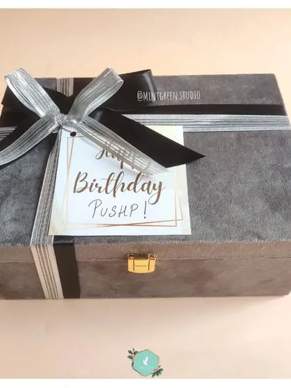 A birthday hamper wrapped in a stylish grey suede box with a silver and black ribbon. The personalized "Happy Birthday" tag adds a special touch to this elegant gift.