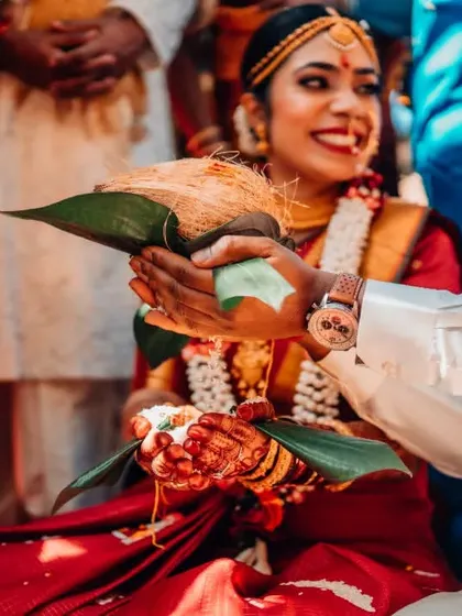A happy, candid moment during a wedding ritual, with the couple sharing a coconut.