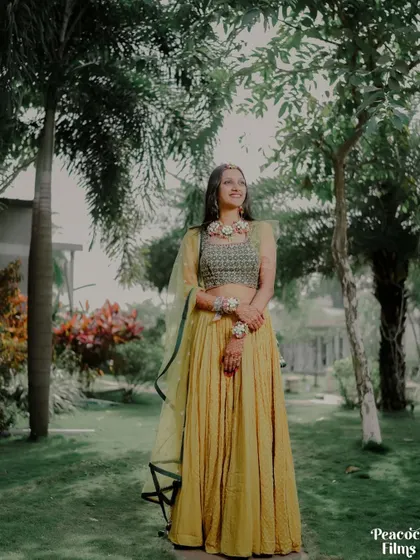 A full-length portrait of the bride in her vibrant yellow Haldi lehenga, standing in a beautiful garden setting.