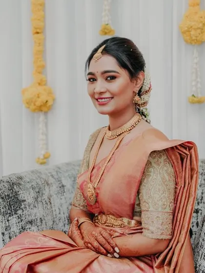 A full-length view of the bride in her peach saree, seated gracefully. The custom blouse and simple jewelry create a soft and romantic bridal look.
