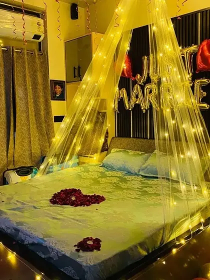 A view of the "Just Married" bed setup with a heart made of rose petals and a fairy light canopy creating a warm, inviting glow.