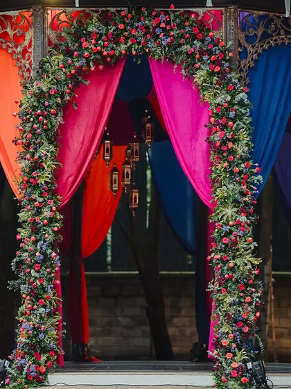 A grand floral arch in shades of red and purple frames the entrance to the main stage, set against the backdrop of colorful drapes.