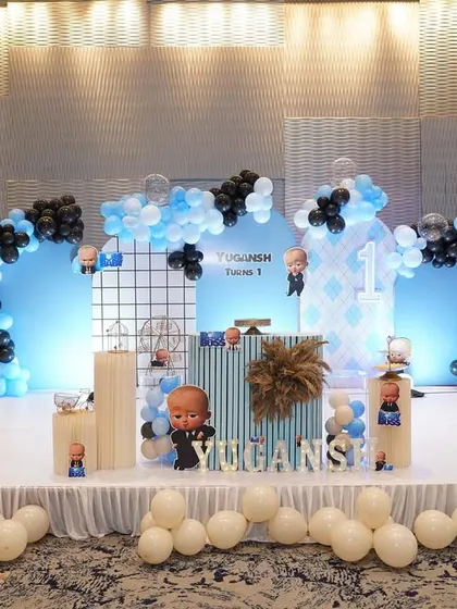 A wide shot of the Boss Baby themed stage. The setup includes a large backdrop, a full balloon arch in black and blue, and a well-decorated stage for the celebration.